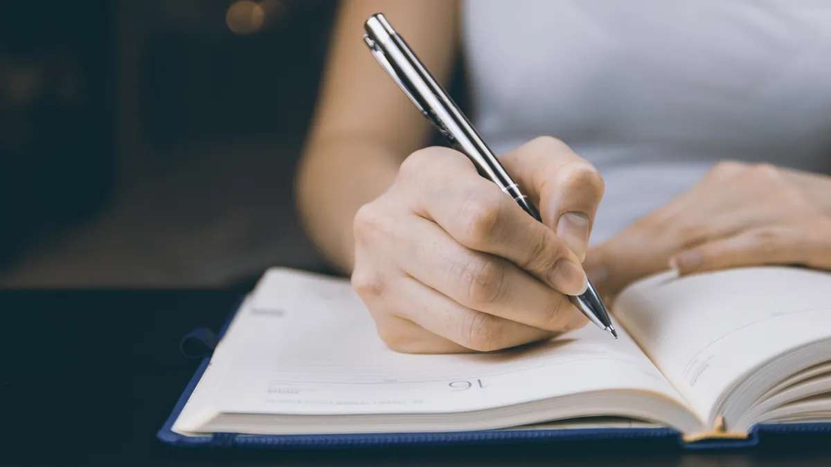 開いた手帳にペンで書き込む手元